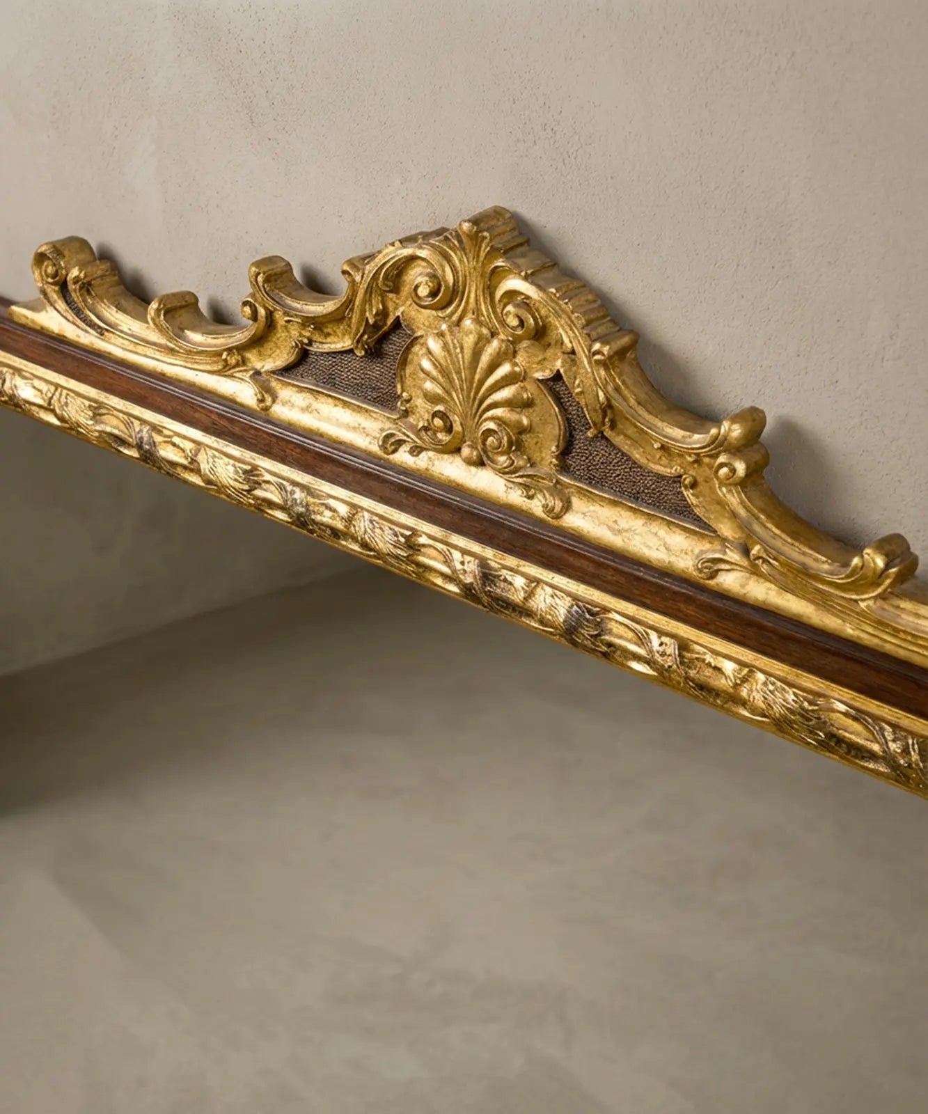 "Detalle de talla en madera dorada con forma de concha y hojas de acanto en la parte superior del espejo."