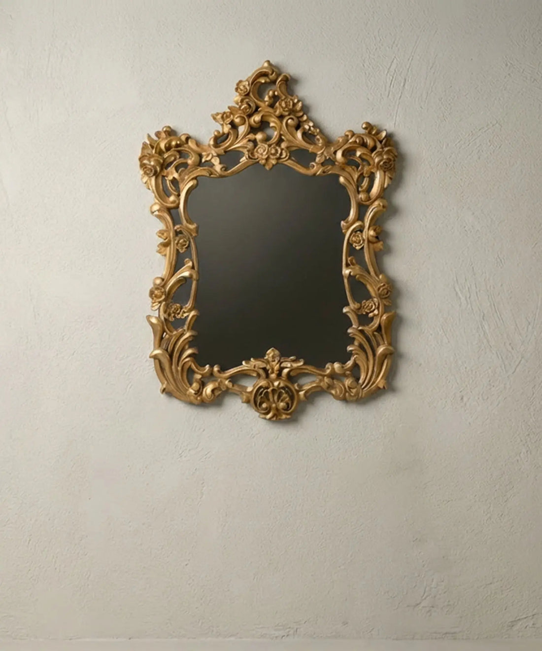 Espejo de pared barroco dorado con tallas florales sobre fondo neutro.