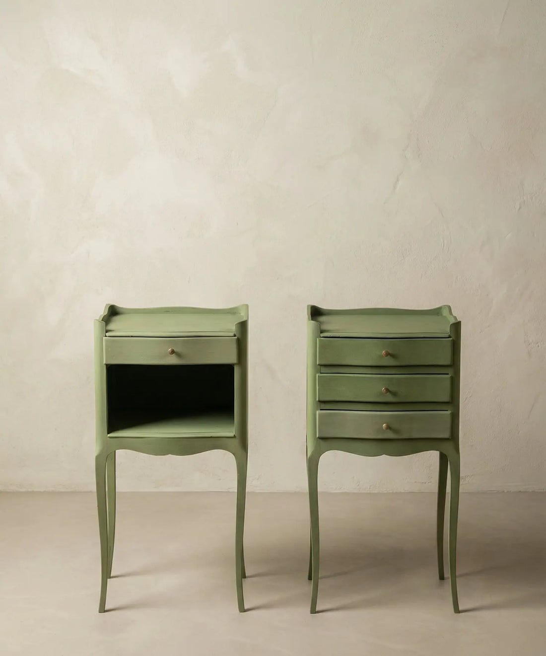 Pareja de mesitas de noche vintage color verde salvia estilo Luis XV sobre fondo neutro.