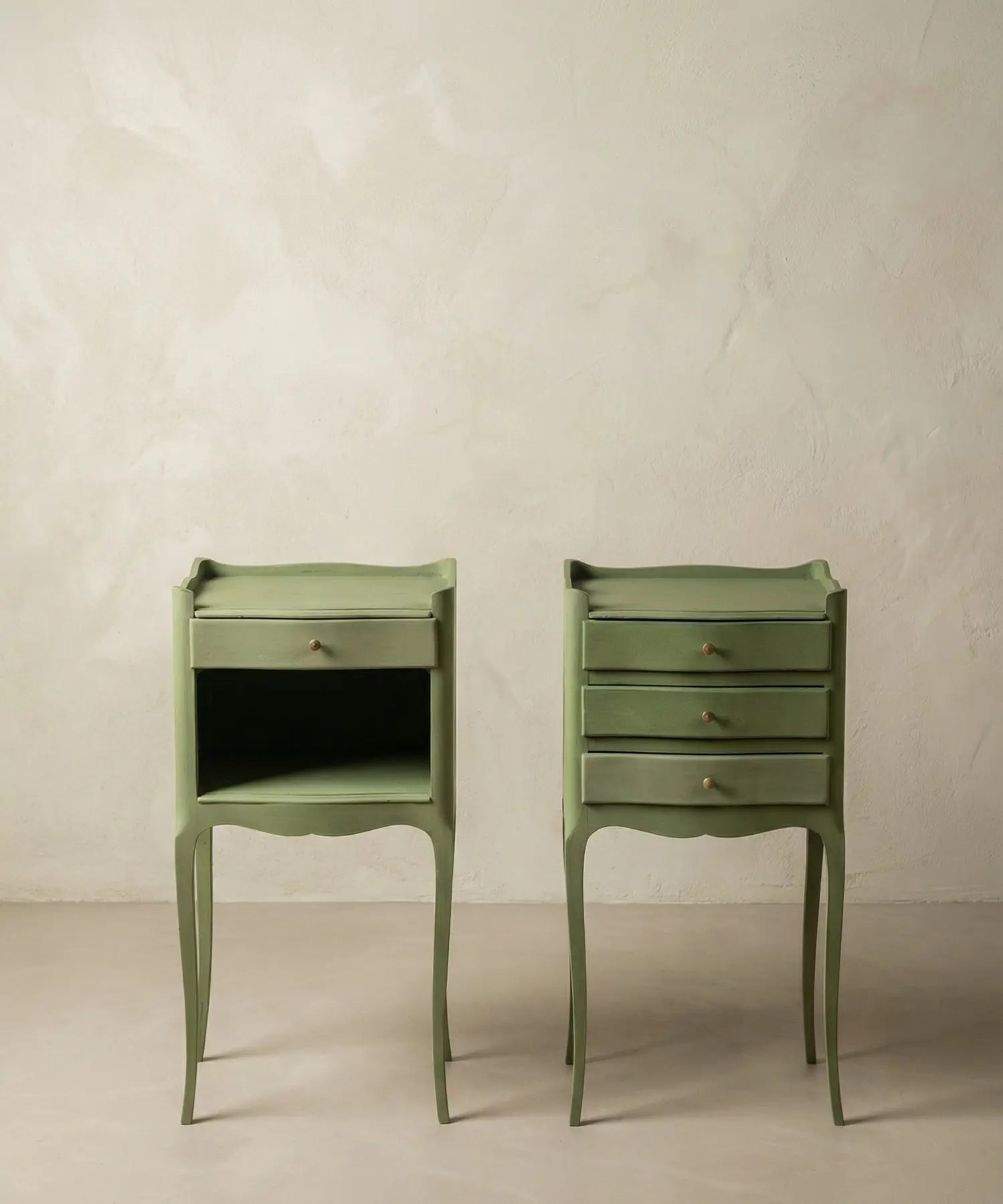 Pareja de mesitas de noche vintage color verde salvia estilo Luis XV sobre fondo neutro.
