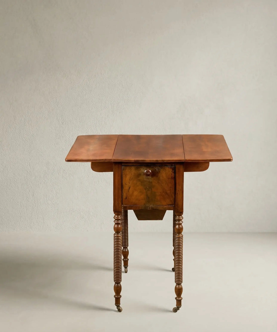 Mesa costurero antigua de caoba estilo Regencia con patas anilladas y ruedas.