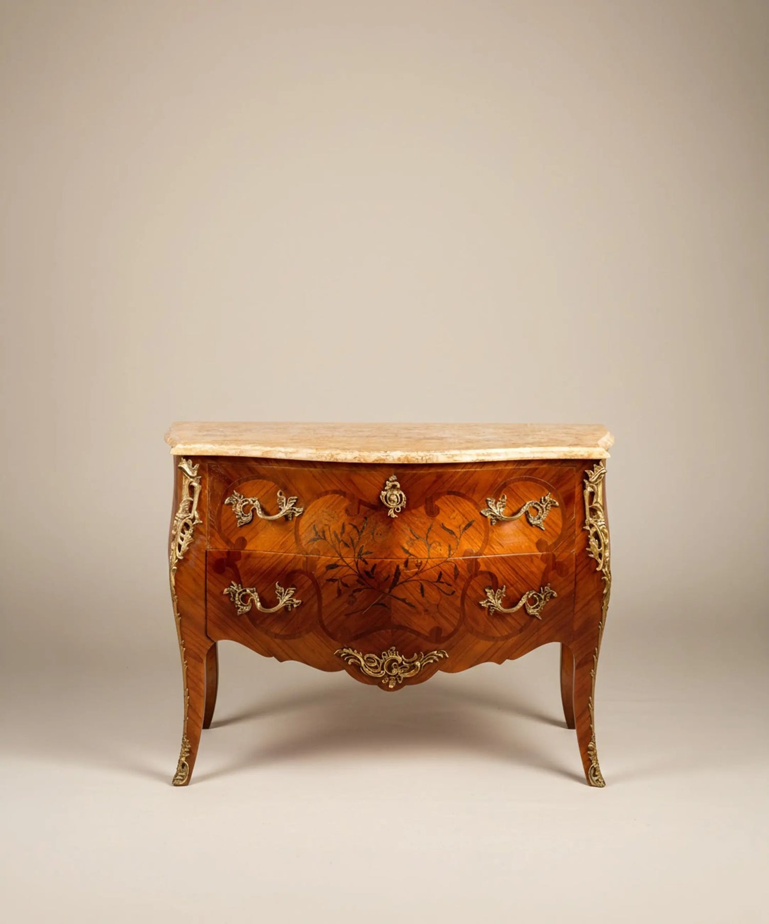 Vista frontal de cómoda bombé estilo Luis XV con marquetería floral y sobre de mármol crema.