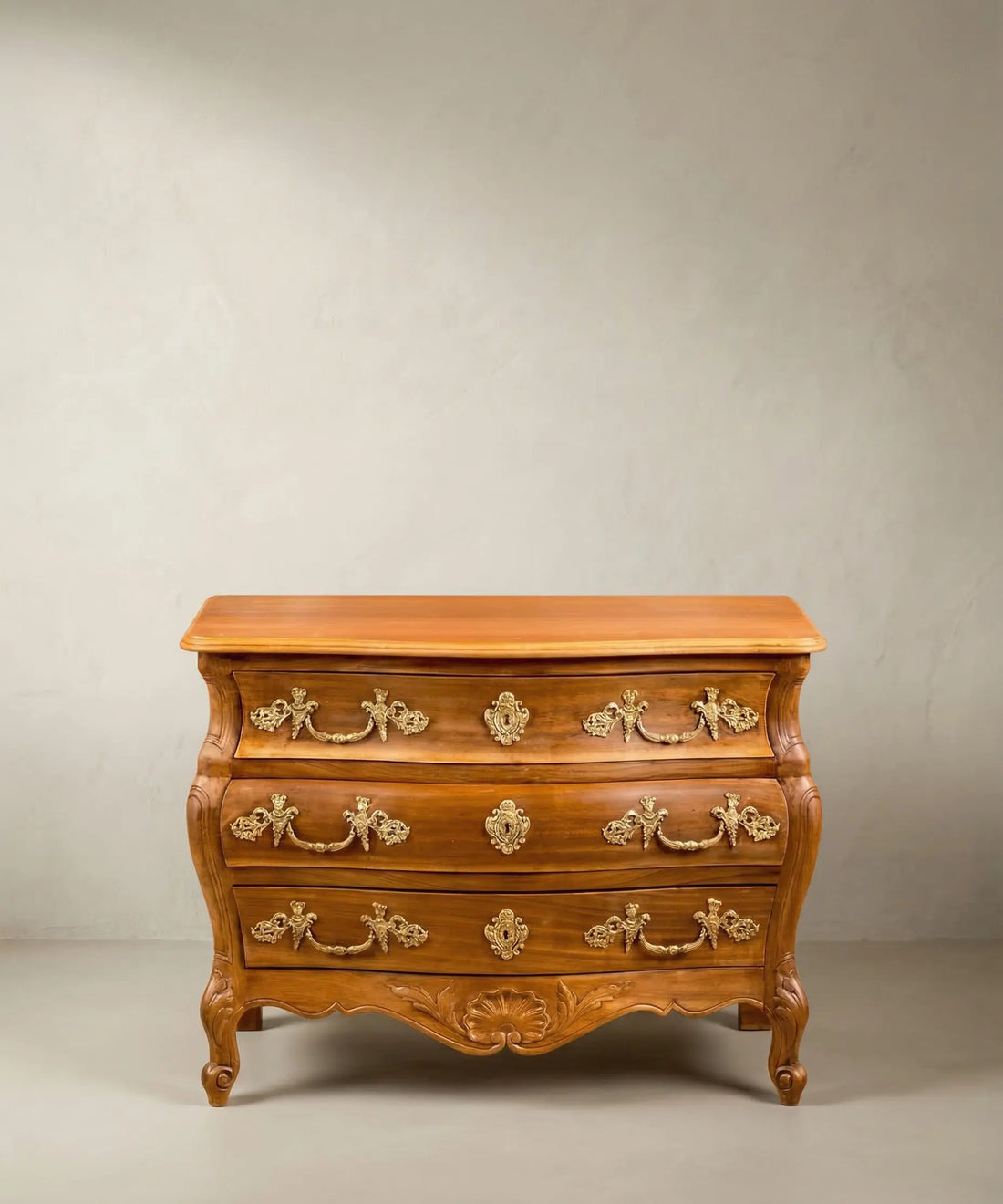 Cómoda bombé vintage de madera estilo Luis XV con bronces dorados y patas curvas.