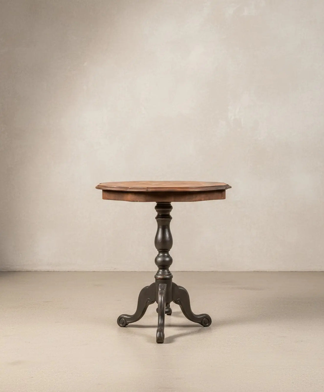 Mesa velador antigua con tablero de marquetería floral y base trípode negra sobre fondo neutro.