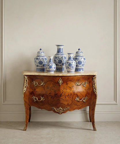 Cómoda Luis XV decorada con jarrones de porcelana azul y blanca en un ambiente de lujo clásico.