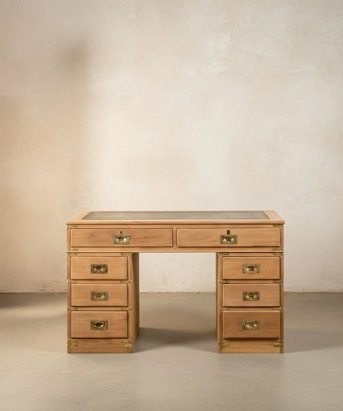 Escritorio de campaña inglés de madera clara con ocho cajones y sobre de cuero verde en ambiente de estudio.