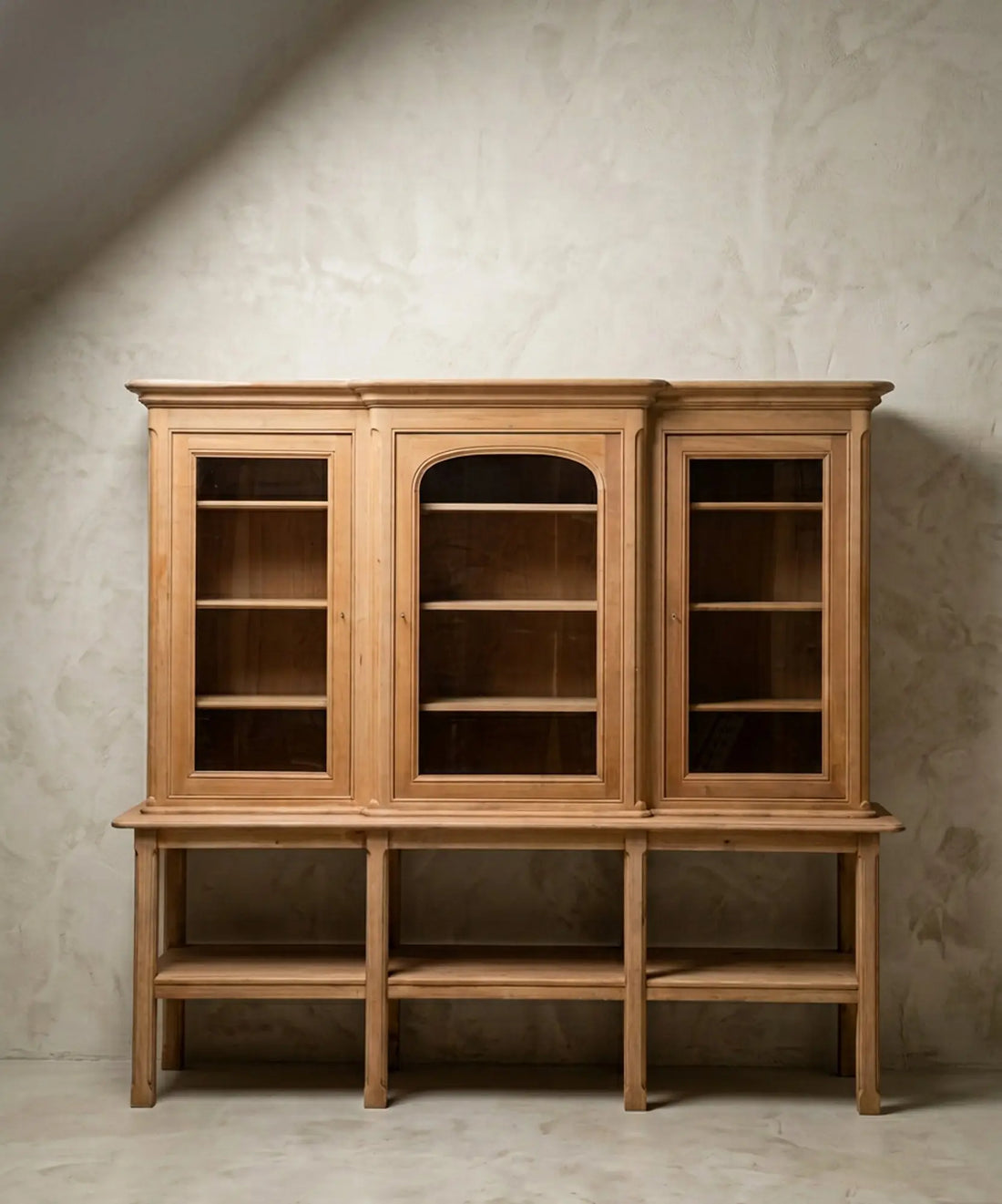 Vista frontal de alacena de tres cuerpos en madera clara natural sobre fondo de pared texturizada gris.