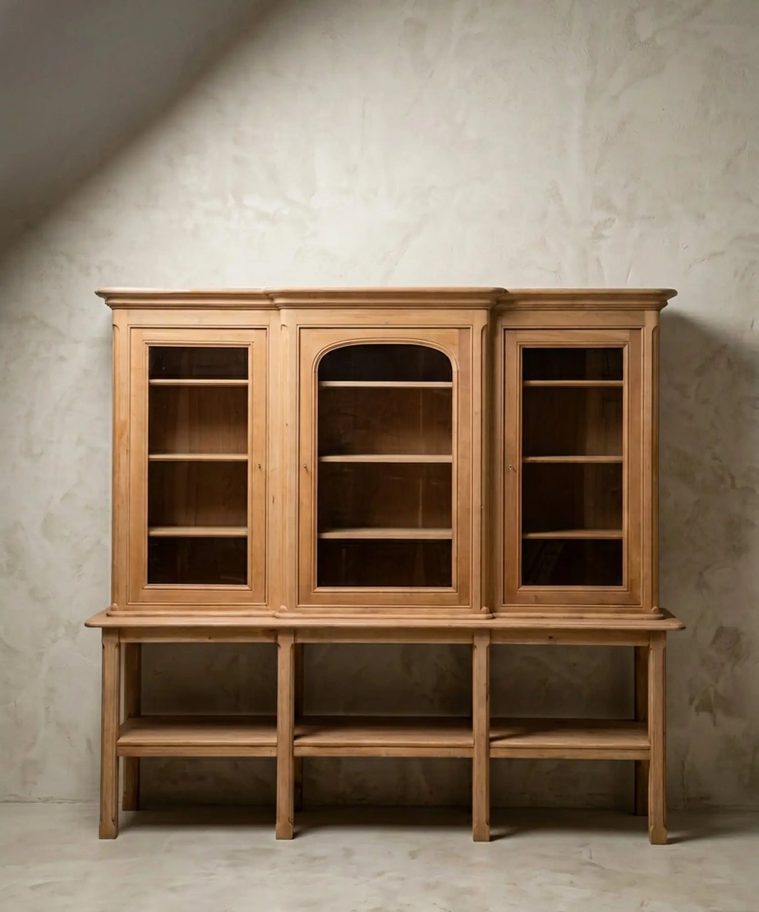 Vista frontal de alacena de tres cuerpos en madera clara natural sobre fondo de pared texturizada gris.