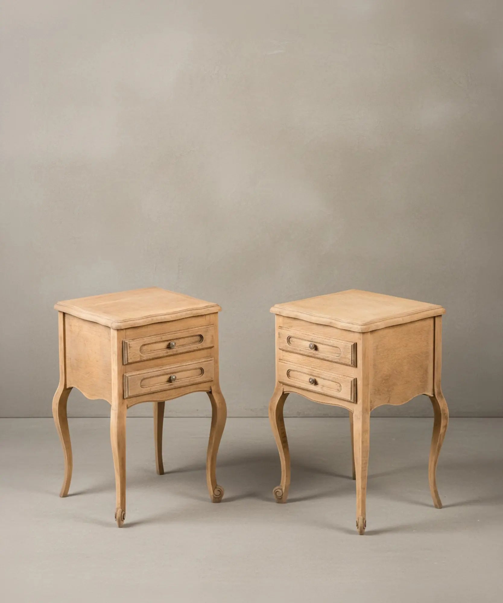 Ángulo lateral de dos mesillas de noche de madera descapada mostrando las curvas de las patas cabriolé.