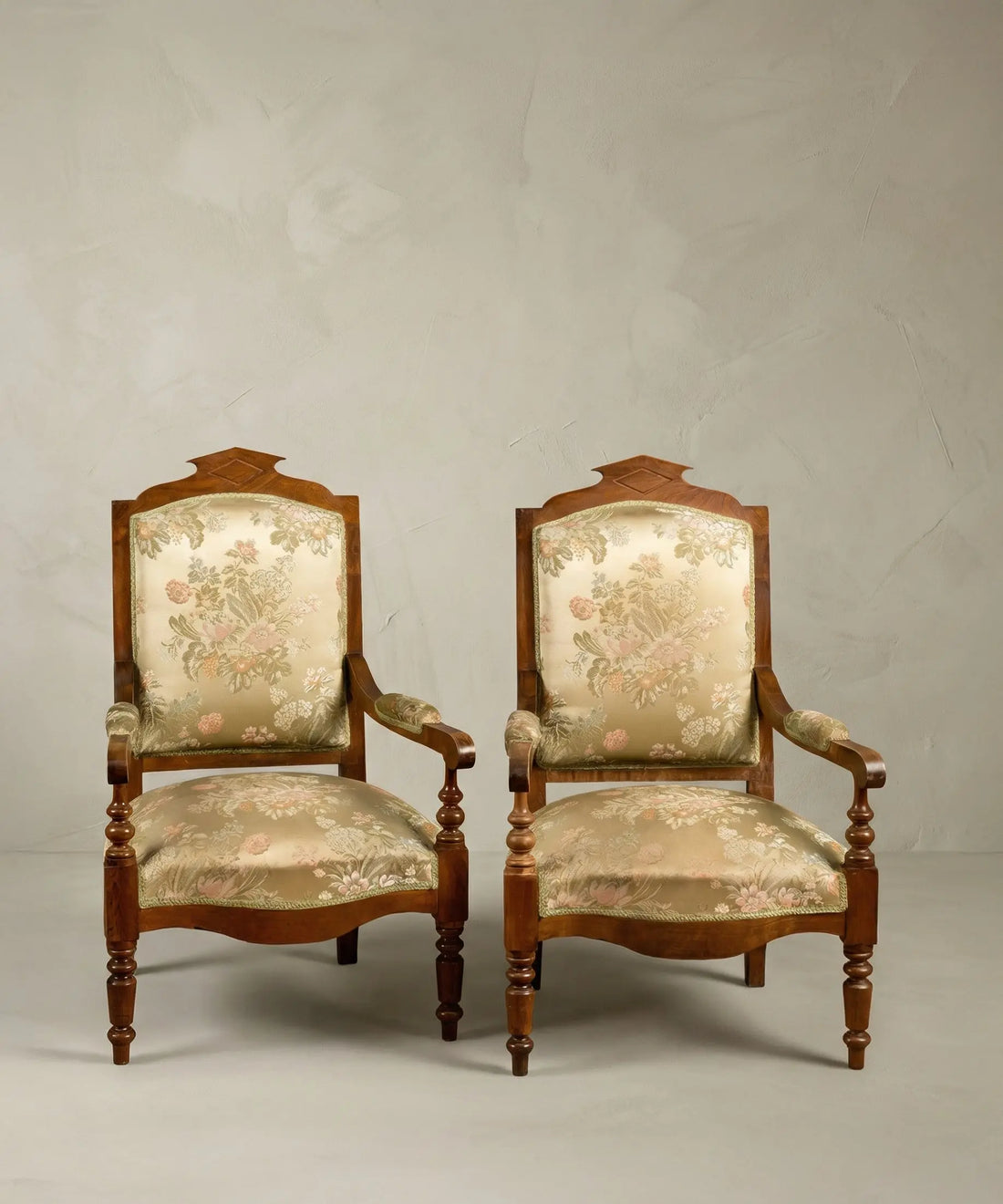 Pareja de sillones antiguos estilo neoclásico con tapicería floral sobre fondo de papel pintado paisajístico sepia.