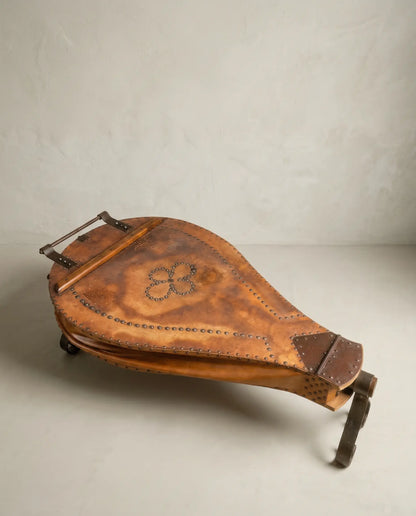 vista superior Mesa de centro fuelle de fragua antiguo en cuero marrón con patas de hierro forjado sobre fondo neutro.