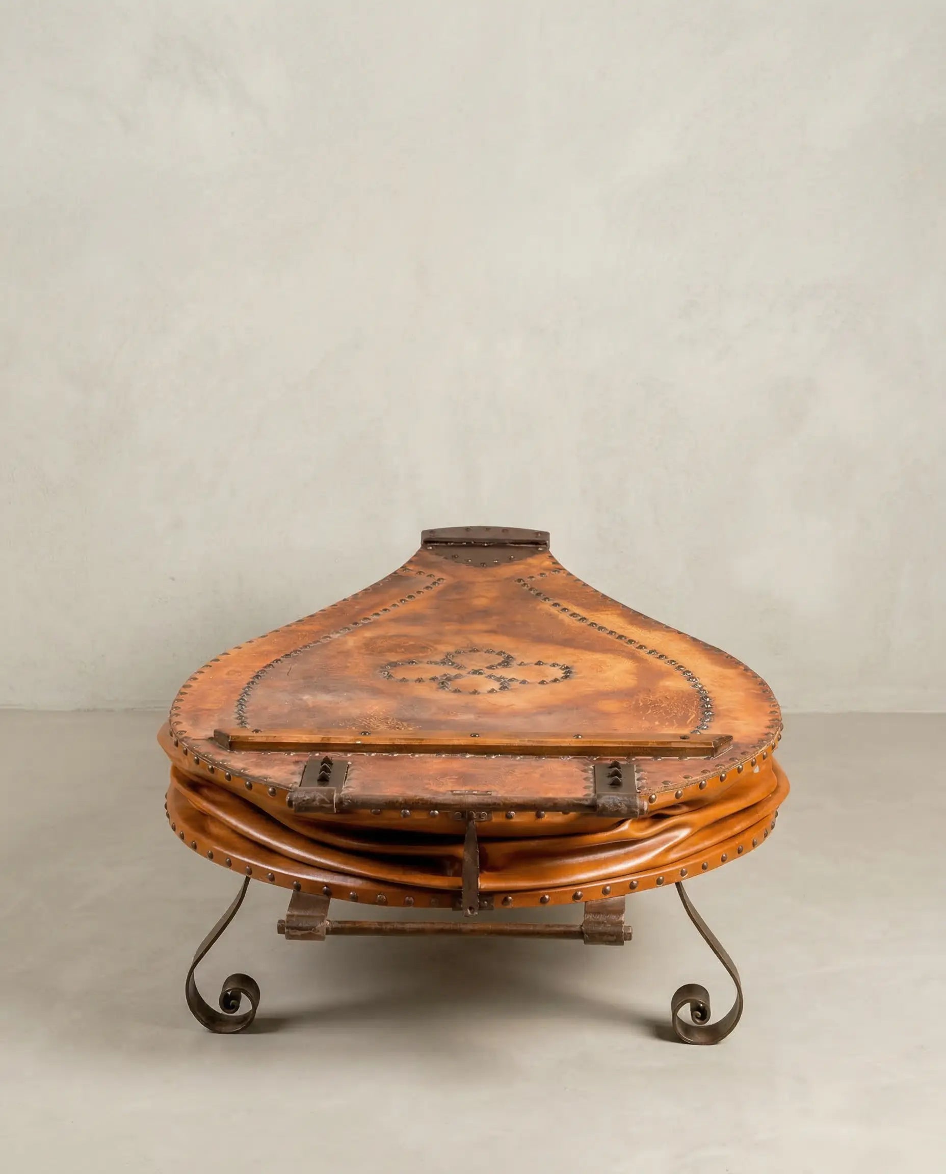 Mesa de centro fuelle de fragua antiguo en cuero marrón con patas de hierro forjado sobre fondo neutro.