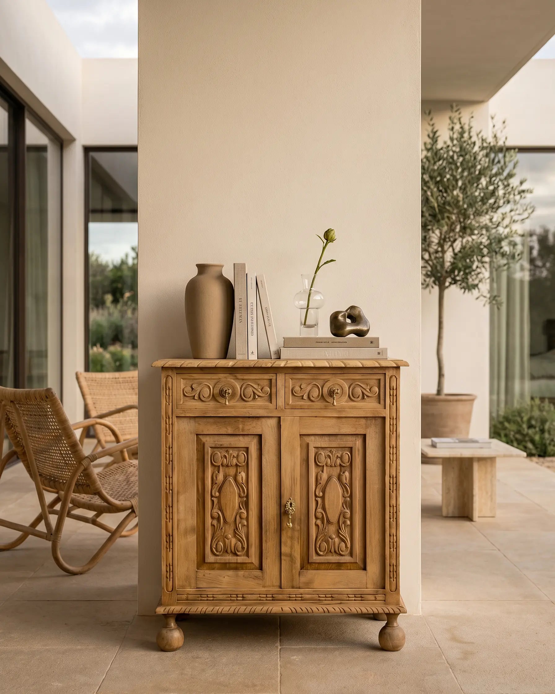 Aparador vintage de madera natural lavada con tallas decorado con jarrones y libros en una terraza moderna