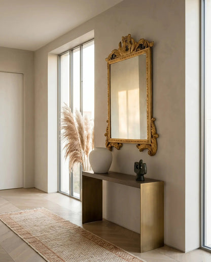 Espejo clásico dorado envejecido decorando un recibidor moderno sobre consola de latón.