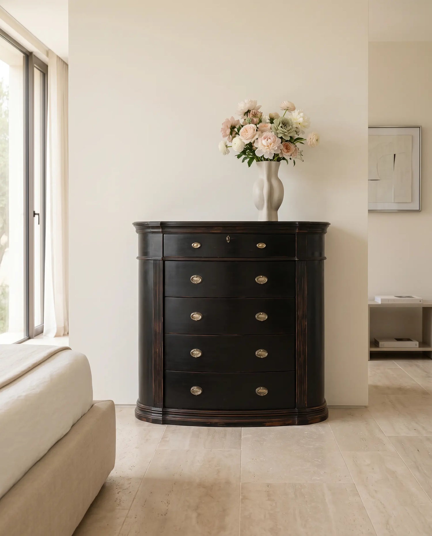 Cómoda negra decapada decorando un dormitorio moderno y luminoso con flores sobre el tablero.