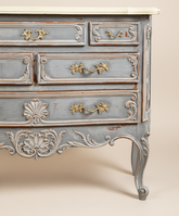 Detalle de las patas cabriolé y los cajones inferiores de una cómoda gris estilo Luis XV con tiradores de bronce.