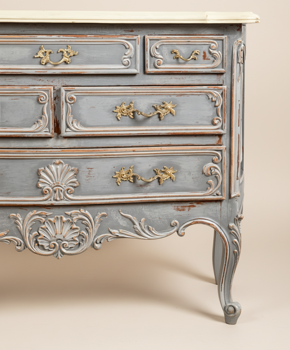 Detalle de las patas cabriolé y los cajones inferiores de una cómoda gris estilo Luis XV con tiradores de bronce.