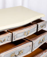 Detalle de las patas cabriolé y los cajones inferiores de una cómoda gris estilo Luis XV con tiradores de bronce.