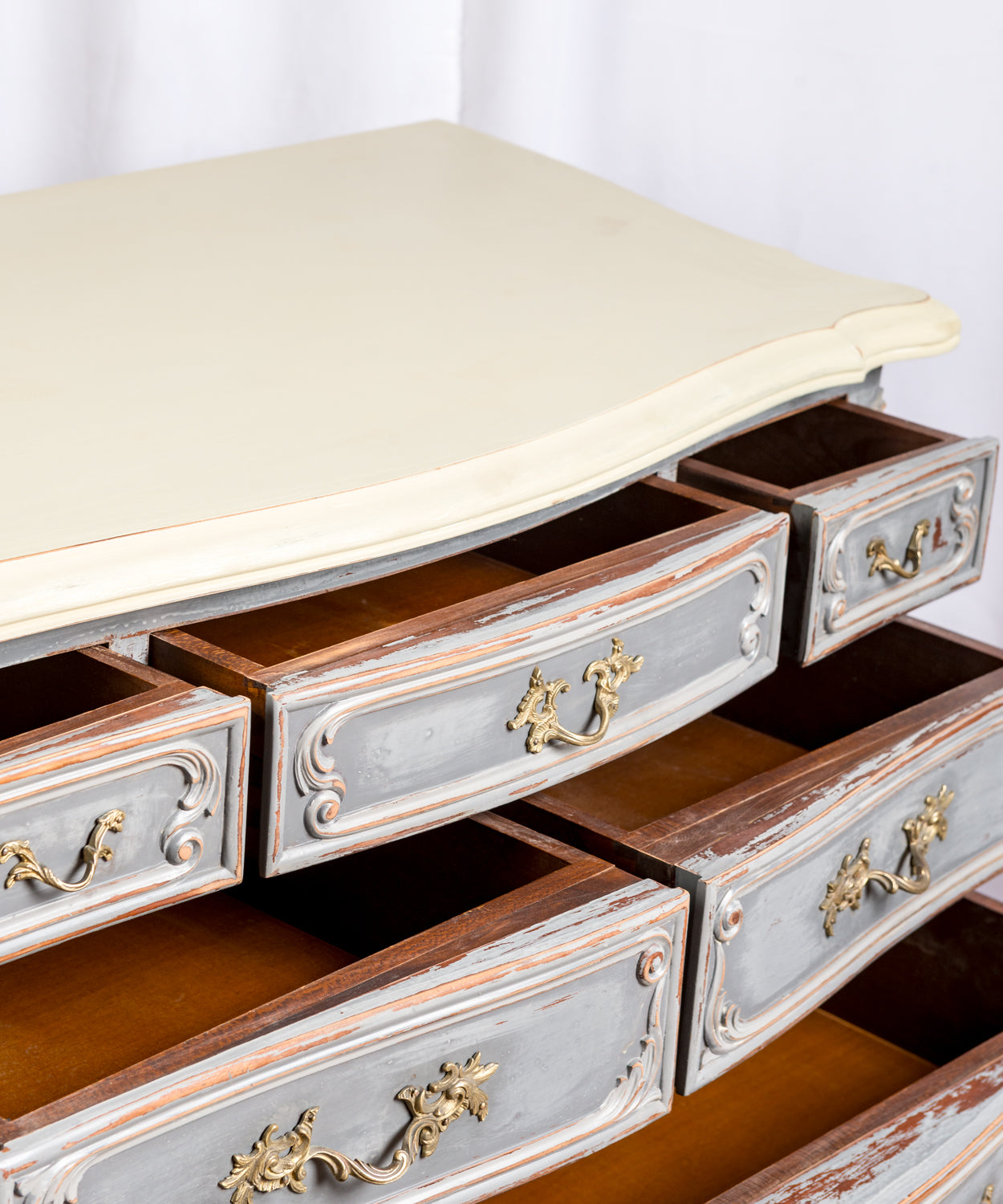 Detalle de las patas cabriolé y los cajones inferiores de una cómoda gris estilo Luis XV con tiradores de bronce.