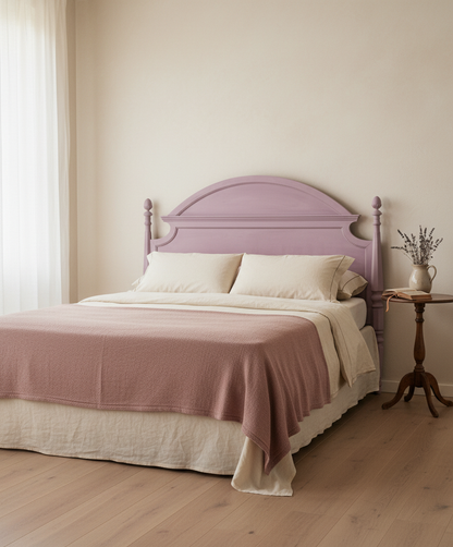 Ambiente de dormitorio luminoso con cabecero rosa, manta de punto color malva y decoración floral seca