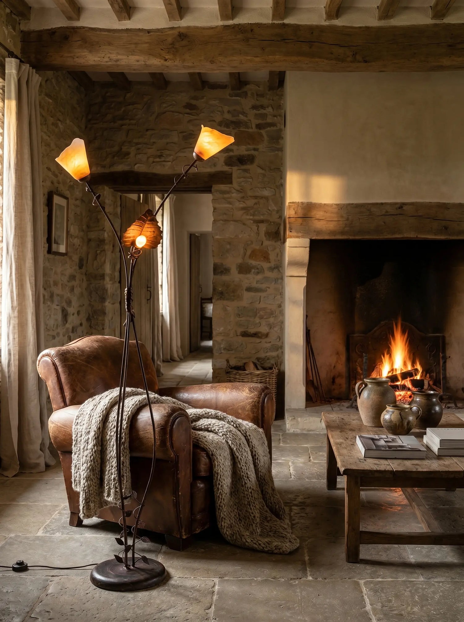 Lámpara de pie de forja encendida iluminando un salón rústico con chimenea y sillón de cuero.