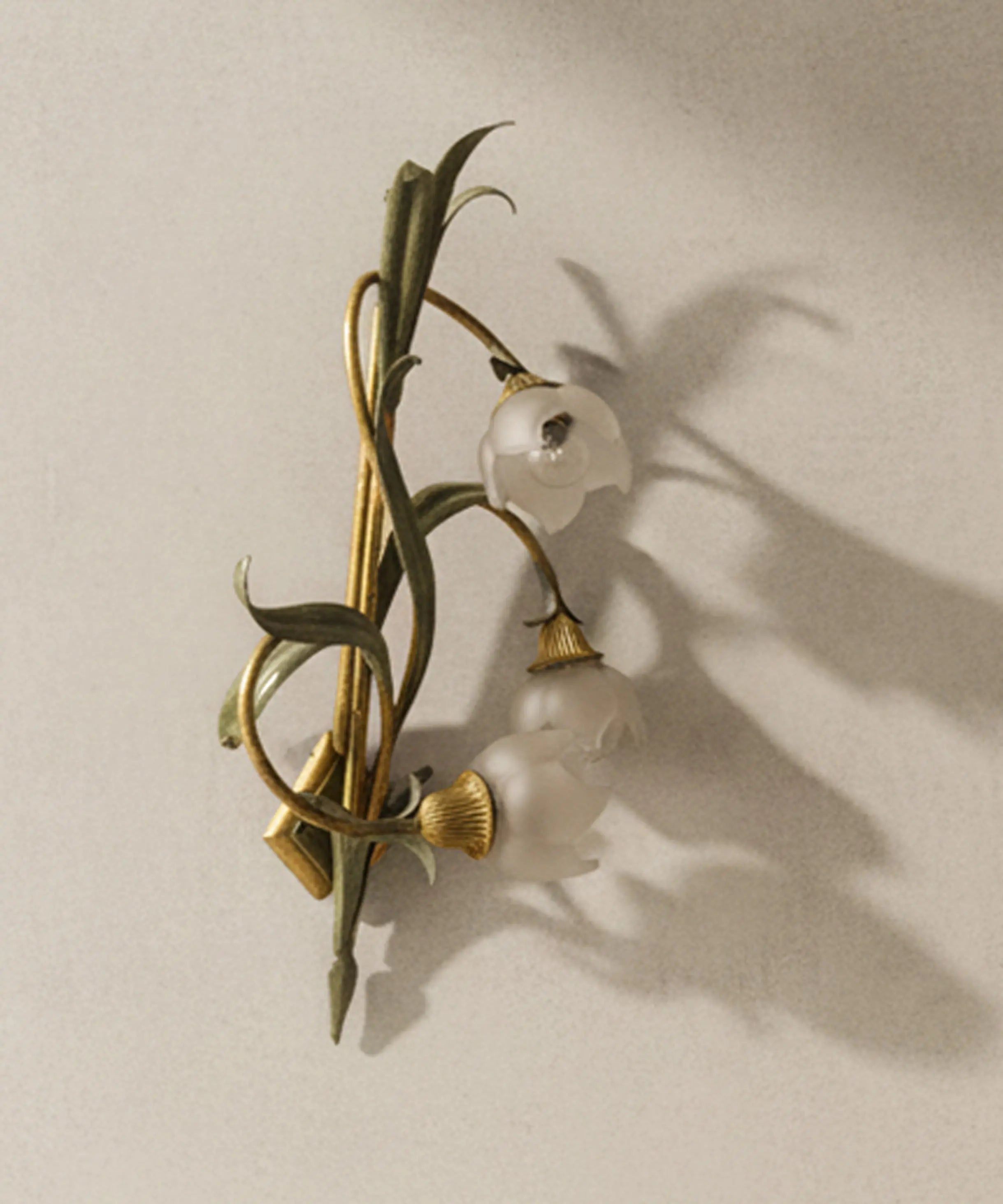 Primer plano de tulipa de cristal esmerilado en forma de flor sobre tallo de forja verde y dorada.