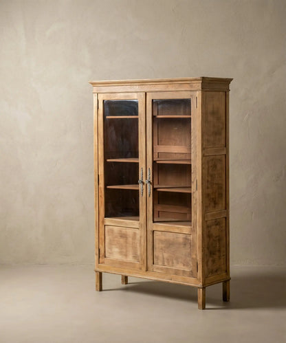 Vitrina de madera clara estilo provenzal con puertas de cristal y herrajes ornamentados sobre fondo neutro.