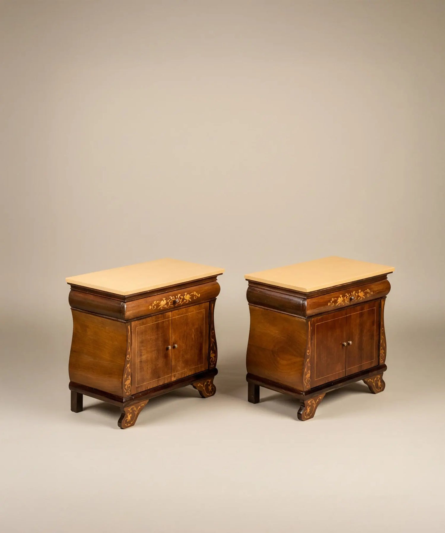 Pareja de mesitas de noche vintage con marquetería de aves y puertas abiertas frente a mural sepia.