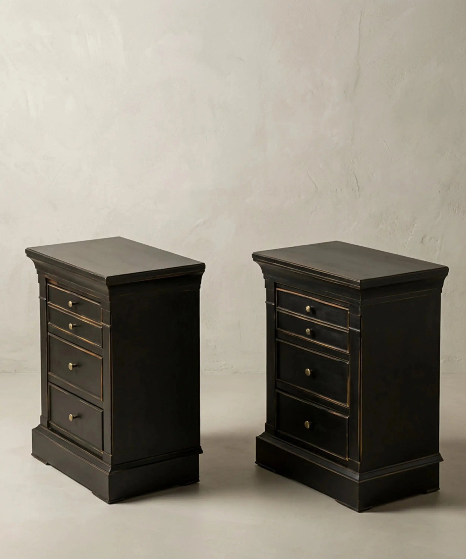 Vista en ángulo de mesitas auxiliares negras con zócalo macizo y tiradores de latón.