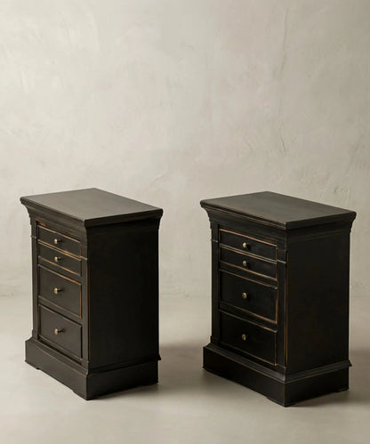 Vista en ángulo de mesitas auxiliares negras con zócalo macizo y tiradores de latón.