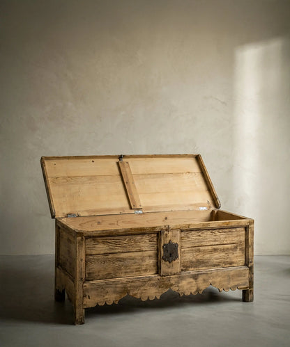 Vista lateral de baúl antiguo de madera clara resaltando la veta natural y estructura robusta.