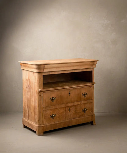  Cómoda antigua de madera clara mostrando el cajón superior oculto en gola y herrajes de bronce.