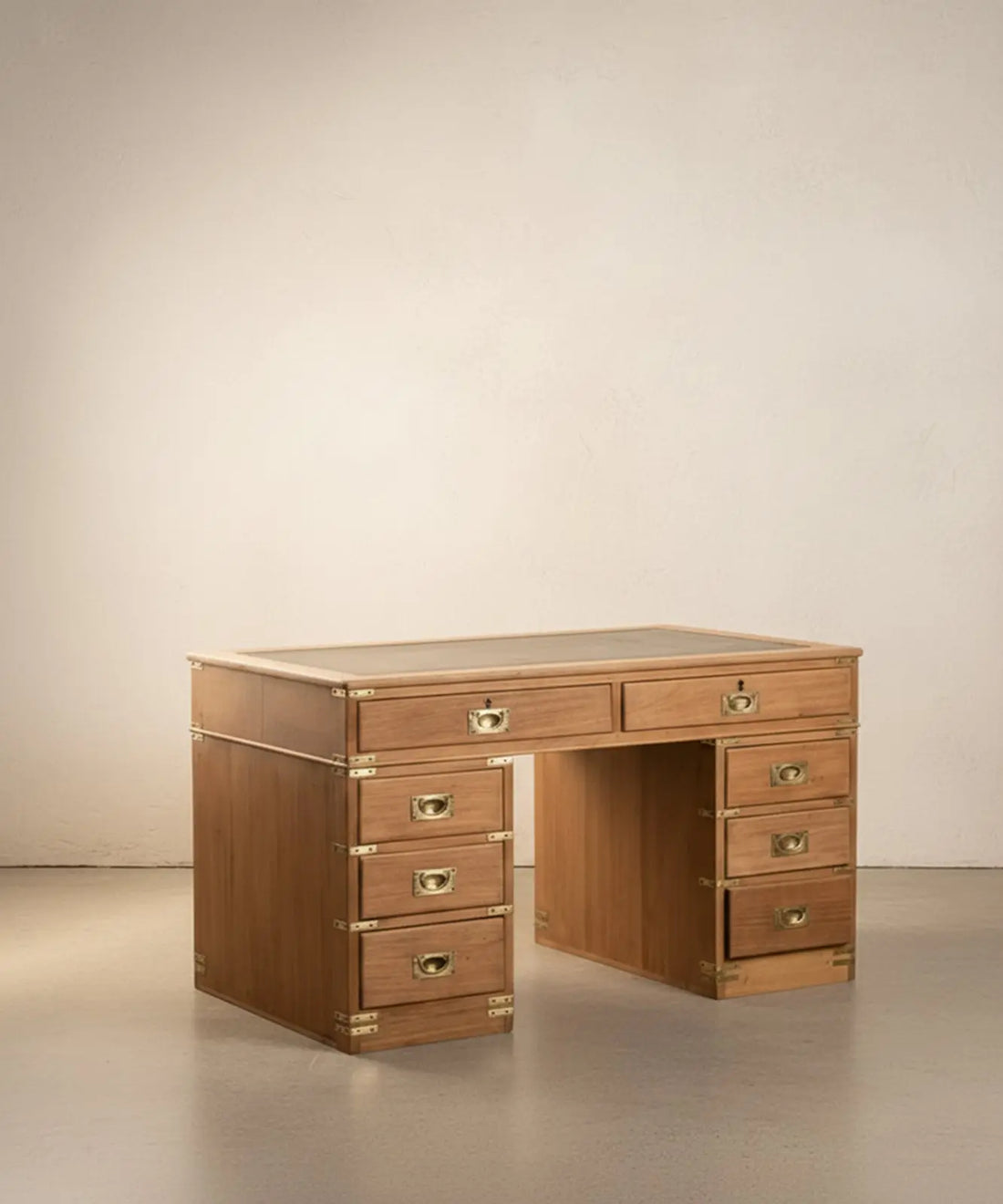 Escritorio de campaña inglés de madera clara con ocho cajones y sobre de cuero verde en ambiente de estudio.