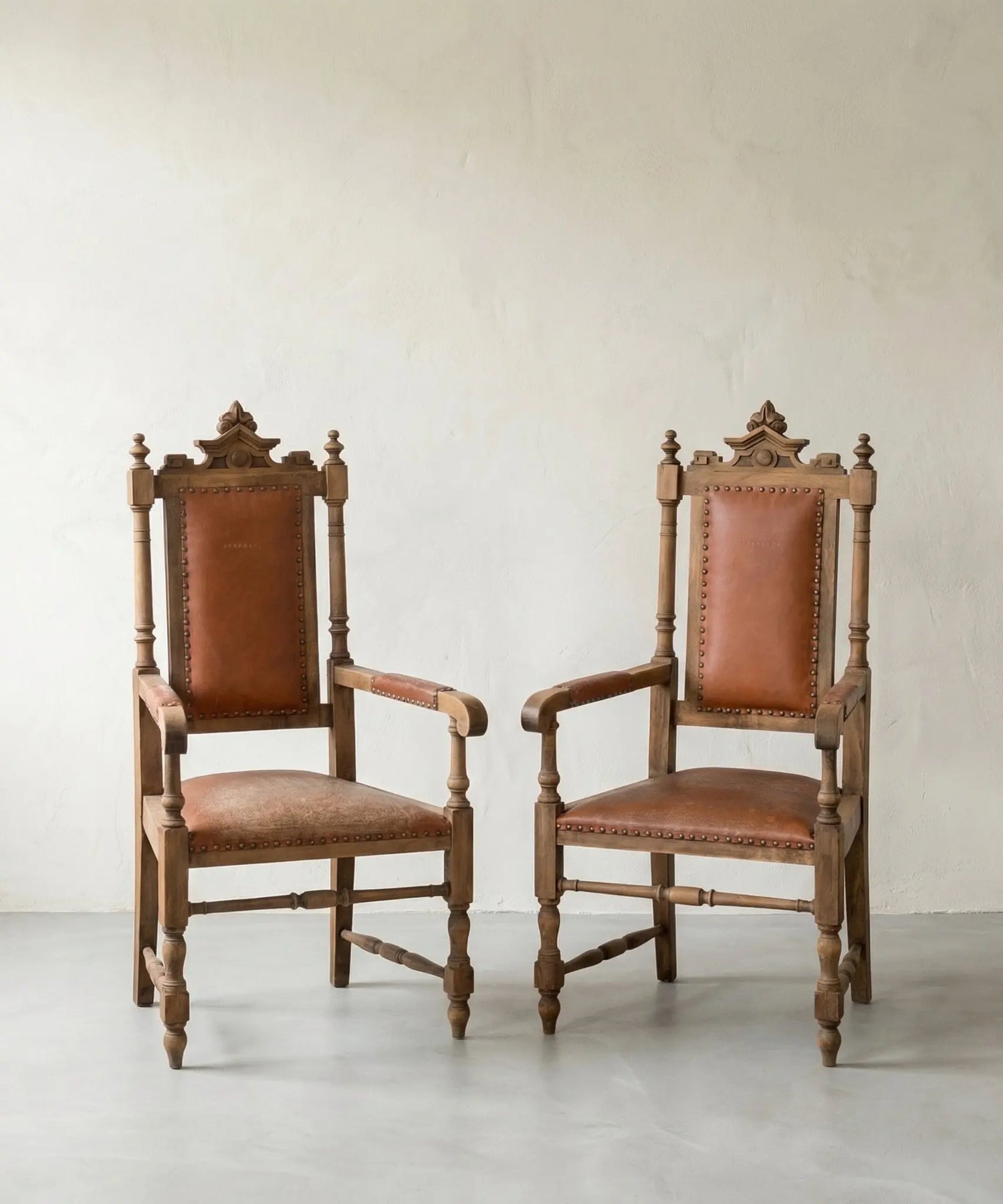 Pareja de sillones fraileros clásicos de madera y cuero marrón con tachuelas.