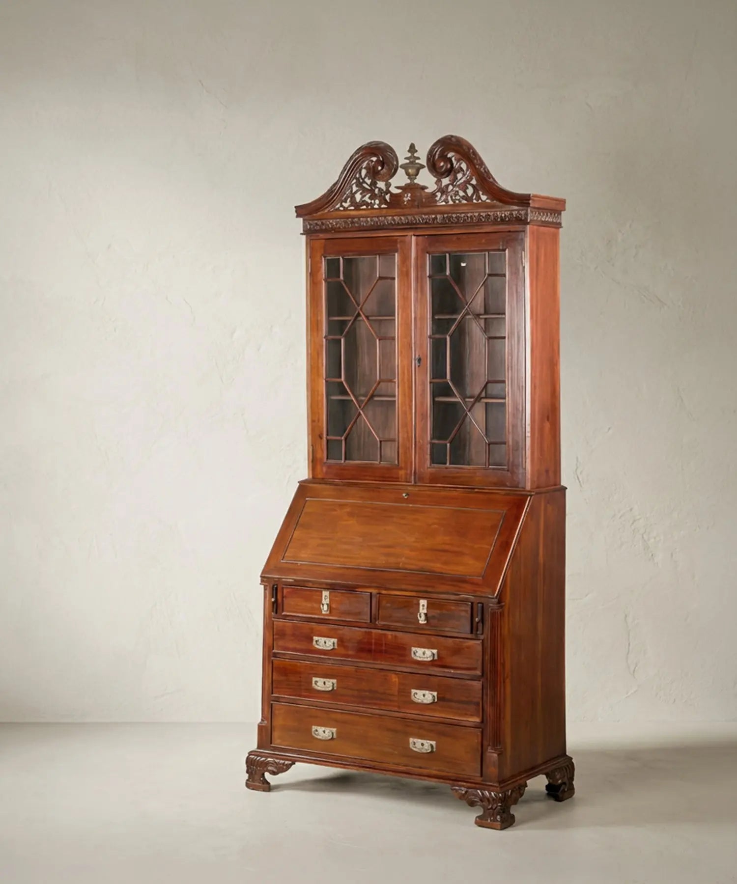 Vista en ángulo del mueble destacando la profundidad de la caoba y el relieve de la talla en el copete superior.