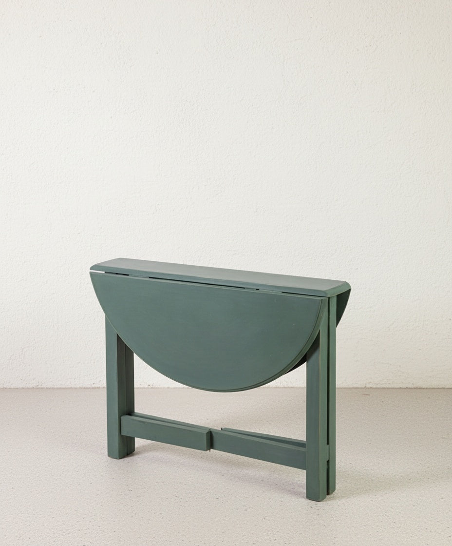 Mesa circular de alas abierta en color verde bosque con base en aspa de madera.