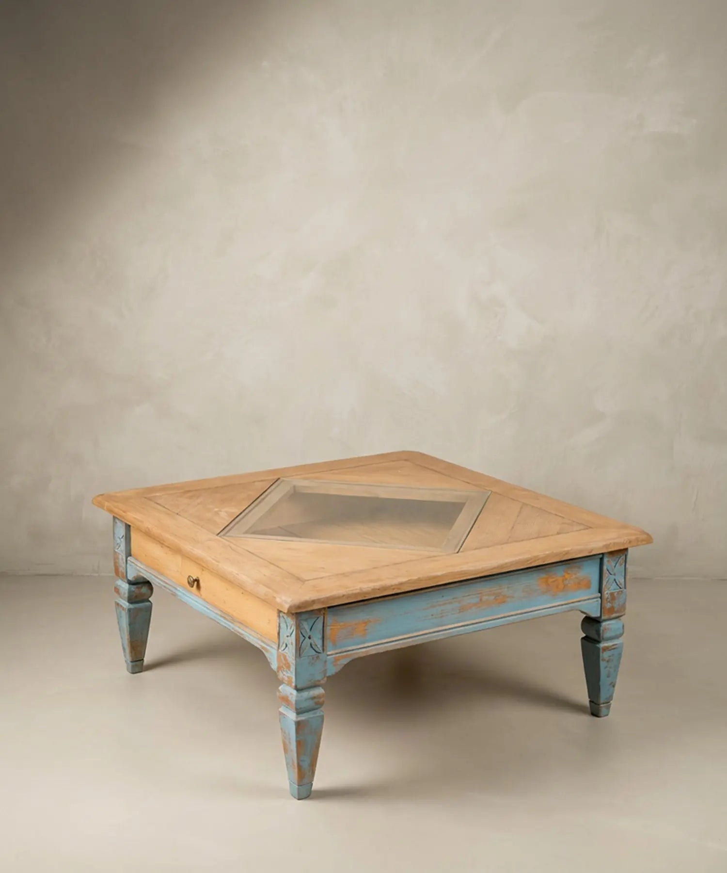 Mesa de centro cuadrada de madera natural con base azul decapado y cristal central.