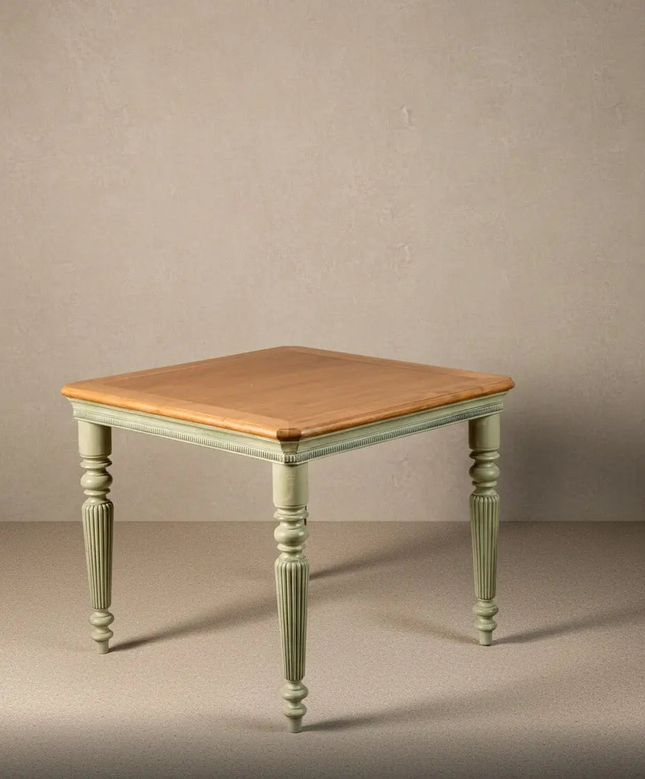 Vista frontal de mesa cuadrada de estilo provenzal con patas acanaladas en color verde musgo y tablero de madera clara natural sobre fondo neutro.