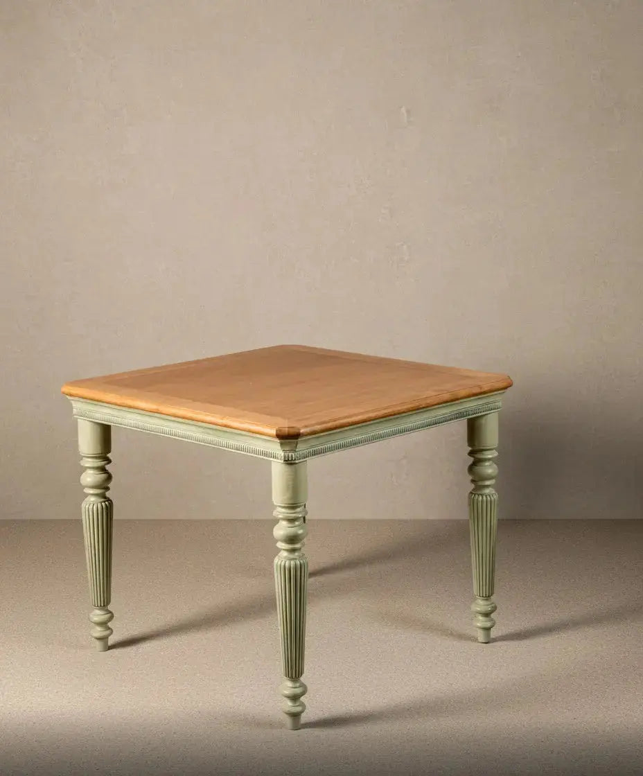 Vista frontal de mesa cuadrada de estilo provenzal con patas acanaladas en color verde musgo y tablero de madera clara natural sobre fondo neutro.
