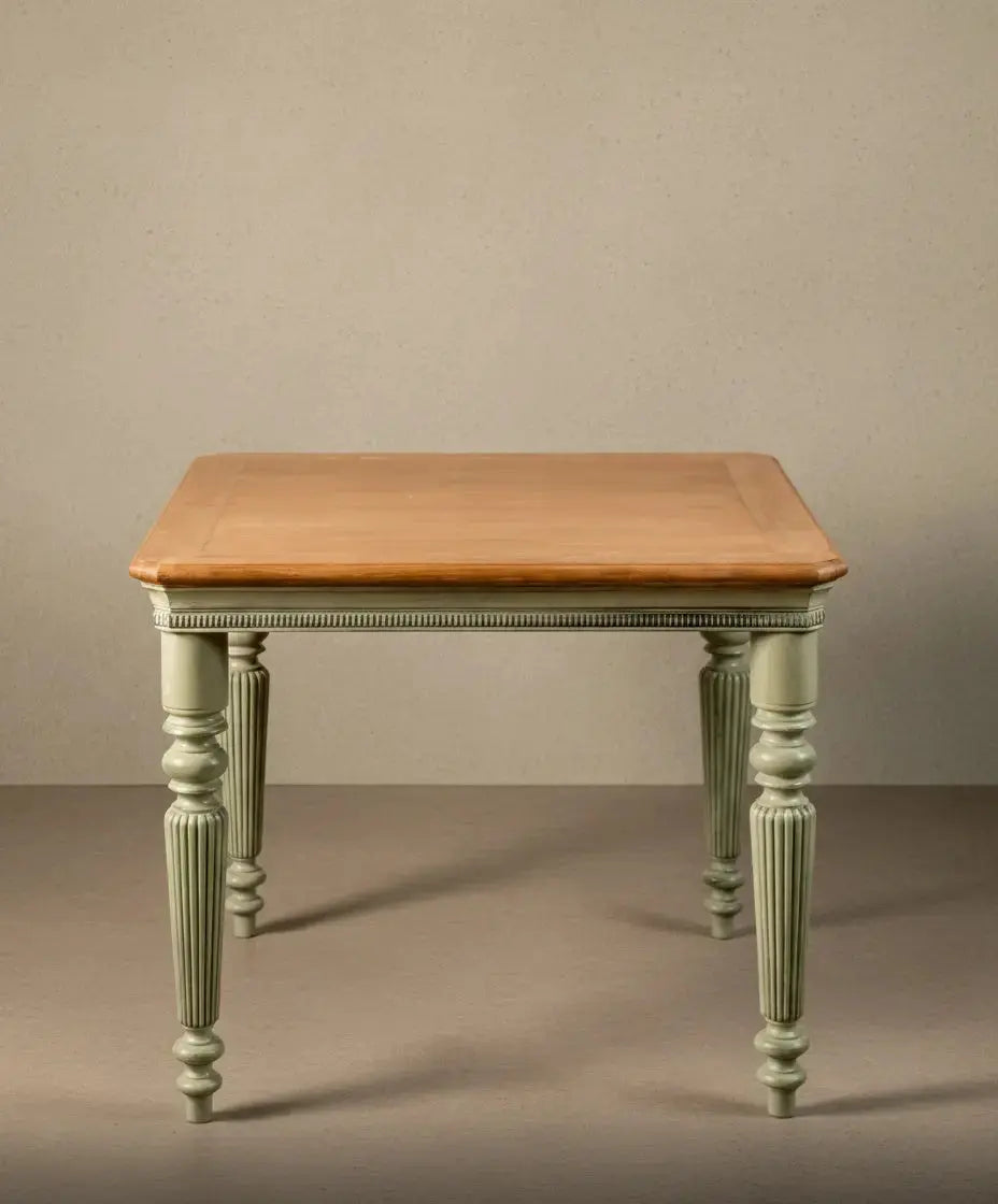 Vista frontal de mesa cuadrada de estilo provenzal con patas acanaladas en color verde musgo y tablero de madera clara natural sobre fondo neutro.