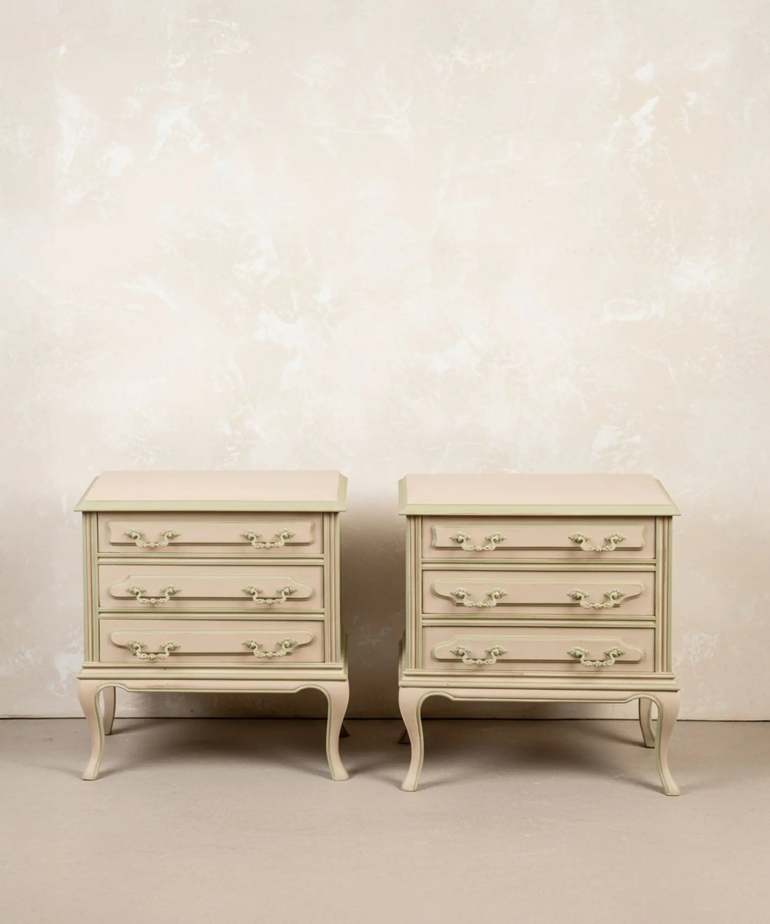 Pareja de mesitas de noche vintage de tres cajones pintadas en beige y verde salvia con patas curvas.