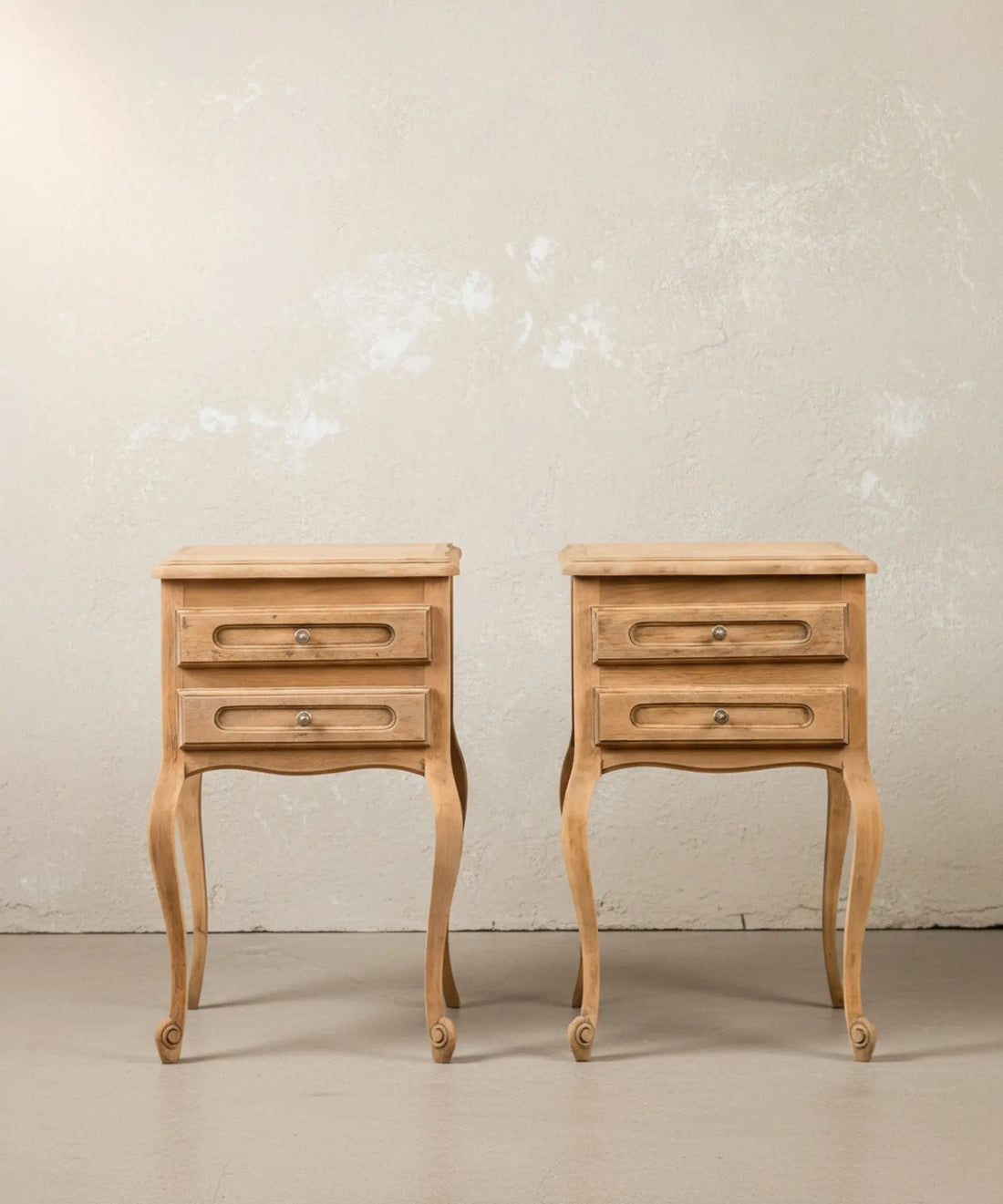 Vista frontal de pareja de mesitas de noche estilo Luis XV en madera clara natural sobre fondo neutro.