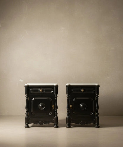 Vista frontal de pareja de mesitas de noche antiguas en negro satinado con encimera de mármol blanco sobre fondo neutro.