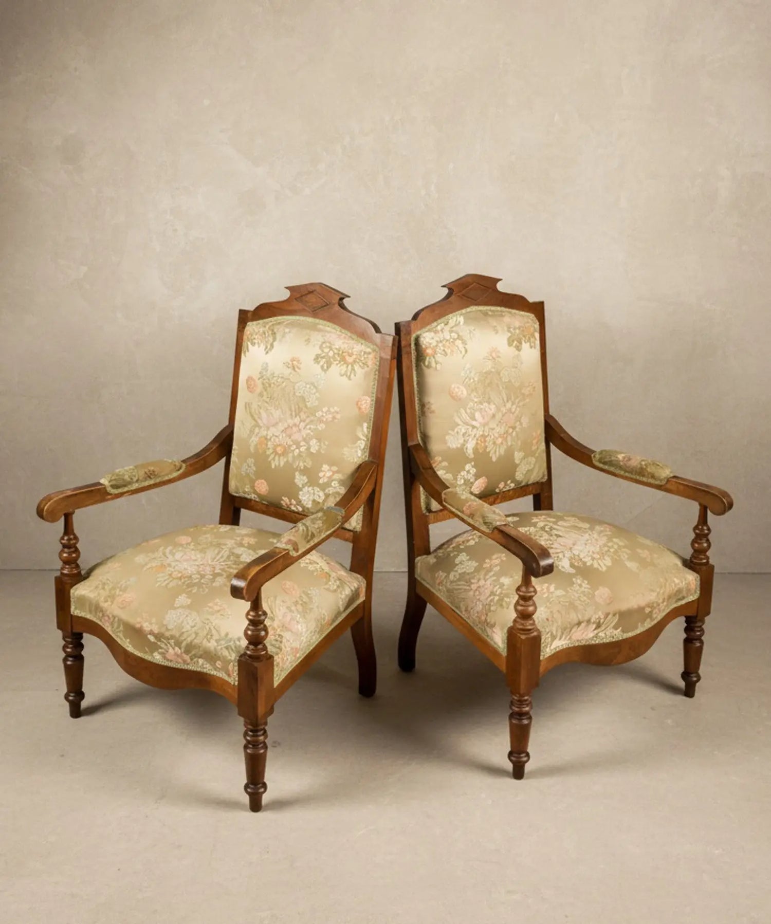 Pareja de sillones antiguos estilo neoclásico con tapicería floral sobre fondo de papel pintado paisajístico sepia.