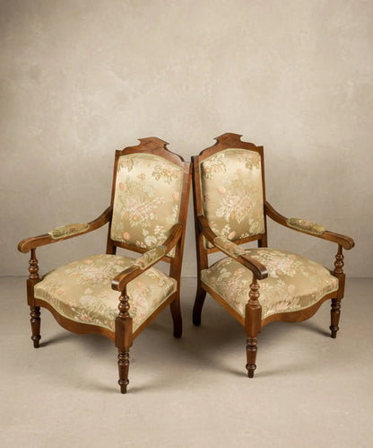 Pareja de sillones antiguos estilo neoclásico con tapicería floral sobre fondo de papel pintado paisajístico sepia.