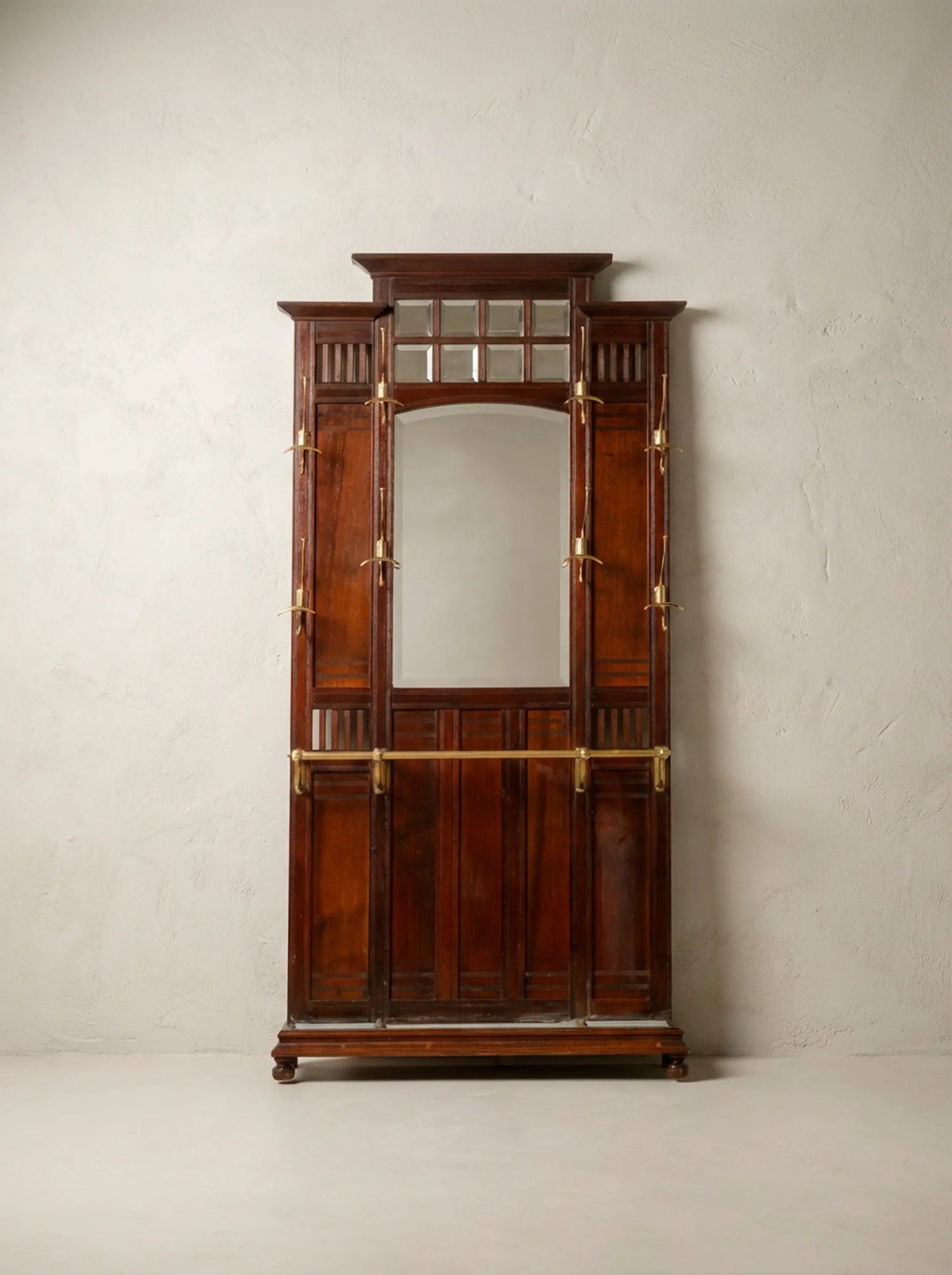 Mueble recibidor antiguo de madera de caoba con espejo central y colgadores de bronce.