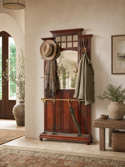 Mueble recibidor antiguo de madera de caoba con espejo central y colgadores de bronce decorando una entrada de casa de estilo mediterraneo