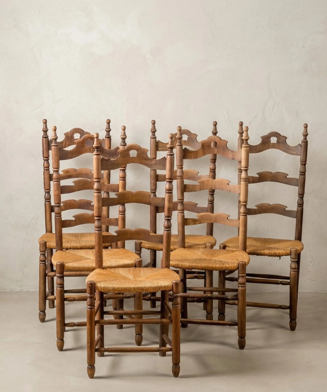 Conjunto de 6 sillas rústicas provenzales vintage en madera y asiento de enea frente a pared clara.
