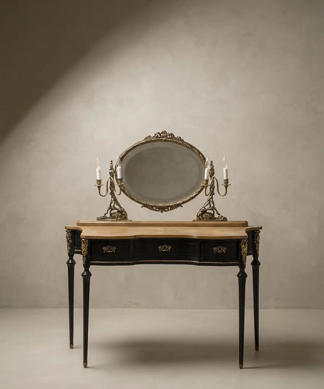 Tocador francés estilo Luis XVI en madera negra y roble con espejo ovalado y luces de candelabro encendidas sobre fondo neutro.