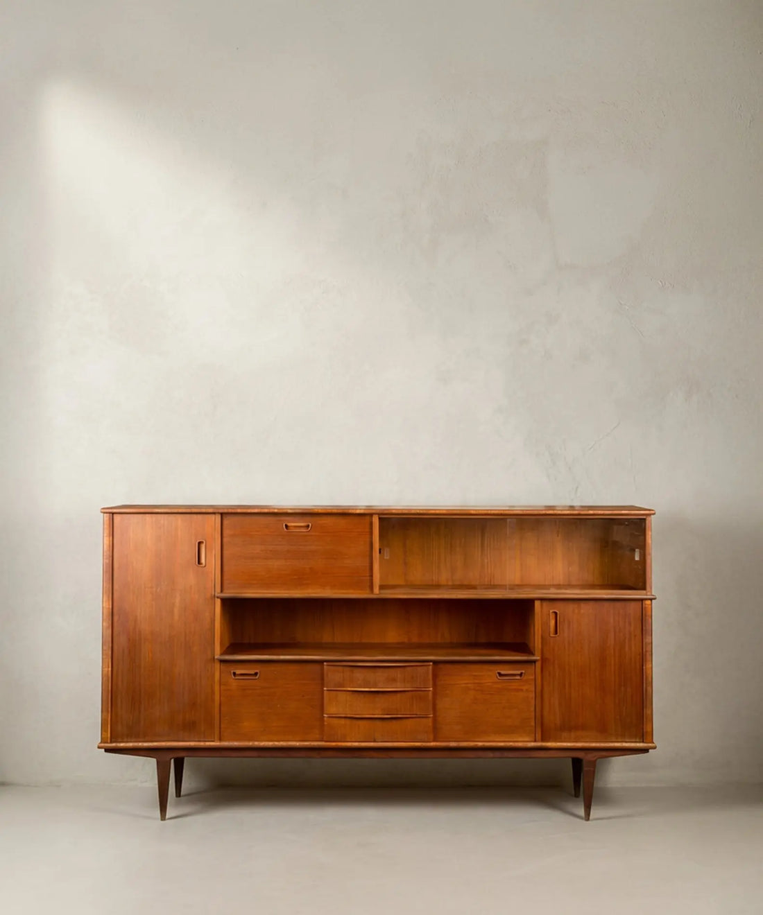 Aparador Mid-Century Modern de teca con puertas y vitrina frontal sobre fondo neutro.